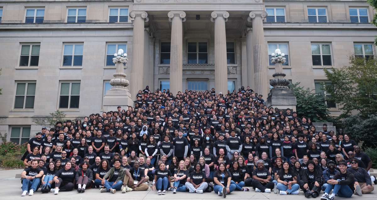 Large group of Science Bound Community in black shirts in front of building. 